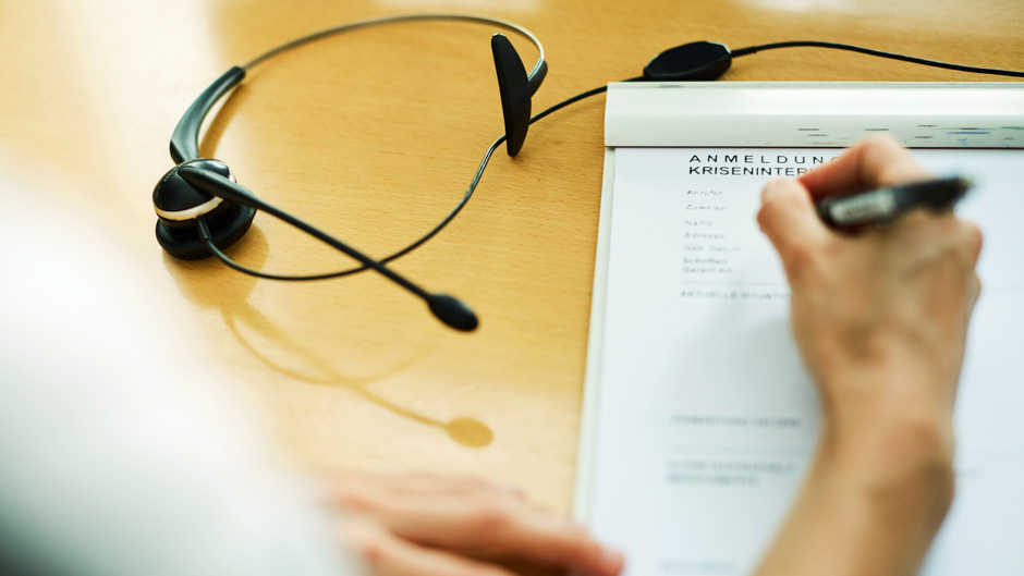 Mitarbeiterin füllt ein Anmeldeformular für die Krisenintervention aus. Daneben ist ein Headphone ersichtlich.